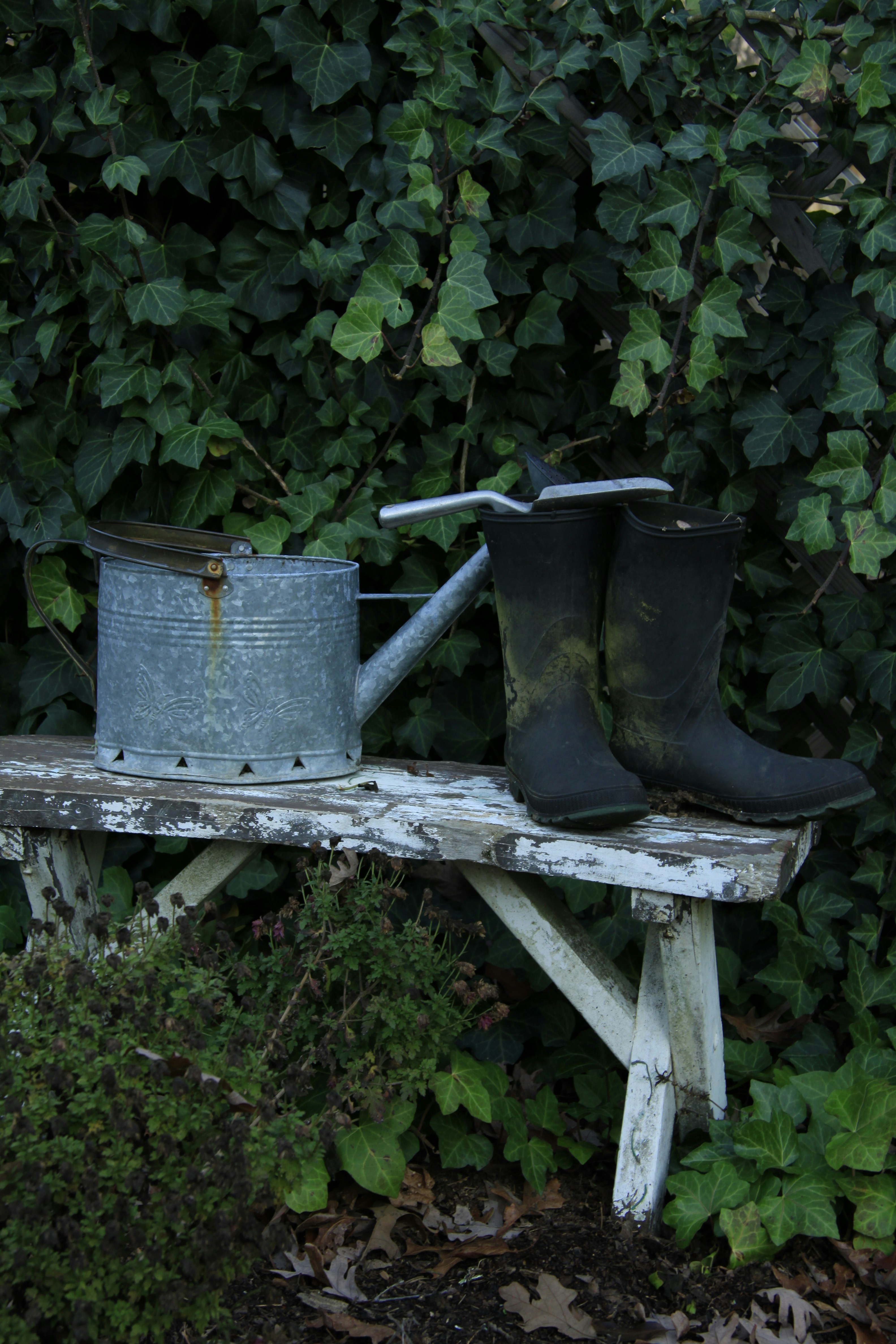 Watering can, muddy boots, and trowel on a weathered bench